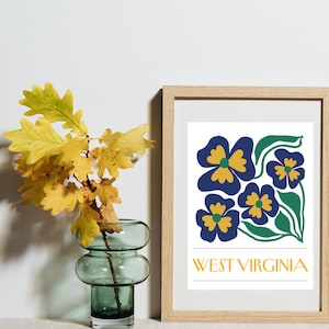 Peut inclure: Une affiche encadrée avec un motif floral de fleurs bleues et jaunes et des feuilles vertes. Le texte "WEST VIRGINIA" est imprimé en dessous. Un vase en verre vert avec des feuilles jaunes est à gauche.