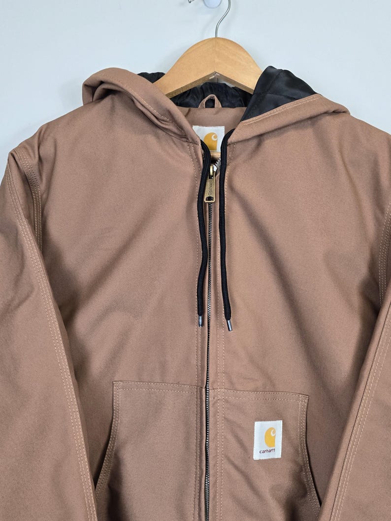 May include: A brown hooded Carhartt jacket with a black zipper and a black drawstring. The jacket has a Carhartt logo patch on the left chest.