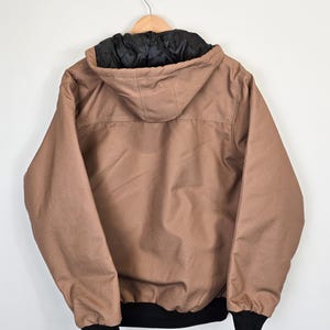 May include: A brown hooded jacket with a black lining and black cuffs. The jacket has a zipper closure and two pockets.