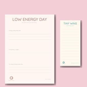 Pode incluir: Dois blocos de notas sobre um fundo rosa. O bloco de notas maior diz "LOW ENERGY DAY" com sugestões de autorreflexão. O bloco de notas menor diz "TINY WINS" com formato de lista. Ambos os blocos de notas são creme com texto verde claro.