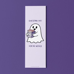 Pode incluir: Marcador de livros retangular com um fantasma de desenho animado segurando livros. O fantasma é branco com olhos pretos e um sorriso. O texto no marcador de livros diz "Ghosting you for my books."