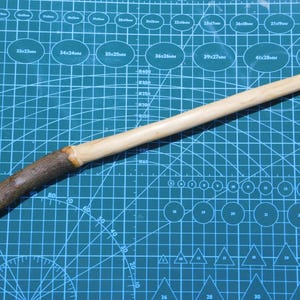 May include: A handcrafted wooden wand. The wand has a light-coloured, smooth shaft and a dark, textured handle. The wand is approximately 30 cm long, suitable for cosplay or magical play.