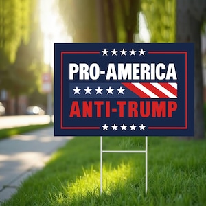 May include: A rectangular yard sign with the text "PRO-AMERICA ANTI-TRUMP" in white and red lettering on a navy blue background. The sign has a red border and is supported by a metal stake, placed in a grassy yard.