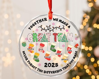 May include: A clear, faceted Christmas ornament with a red ribbon. The ornament features the text "TOGETHER WE MAKE A GREAT TEAM" and "NEVER FORGET THE DIFFERENCE THAT YOU MAKE" with names and the year 2025.