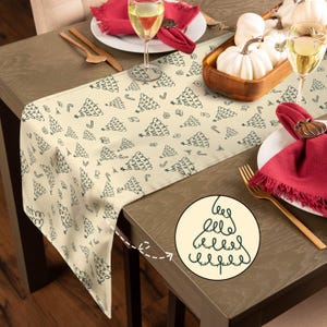 Peut inclure: Chemin de table crème avec un motif répété d'arbres de Noël, de cadeaux et de cannes en noir. Le chemin de table est présenté sur une table en bois, avec des décorations et de la vaisselle festives.