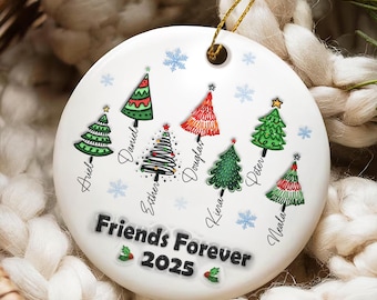 May include: A white ceramic Christmas ornament with a gold string. The ornament features colorful Christmas trees and names, with the text "Friends Forever 2025". Snowflakes and holly accents complete the design.