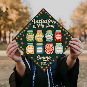 May include: A graduation cap with the phrase "Inclusion is My Jam" and the name "Emma" with the year "2026". The cap is decorated with colorful jars labeled with words like "Diversity", "Acceptance", and "Empathy".