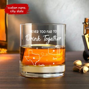 May include: A clear glass with the text "Never too far to drink together" etched on the front. The glass features a map of Texas and Oklahoma with the cities "Lucille" and "Sara" marked. The glass is filled with a golden liquid.
