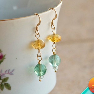 May include: Gold earrings with a teardrop-shaped green and blue gemstone and a round yellow gemstone.