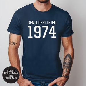 Pu&ograve; includere: Una t-shirt blu navy con testo bianco che recita "GEN X CERTIFIED 1974".