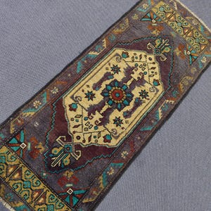 May include: A rectangular, vintage-style rug with a central beige medallion featuring a floral design in teal, red, and brown. The rug has a dark purple background with teal and gold borders, showcasing an intricate pattern. The rug is approximately 36 inches long.