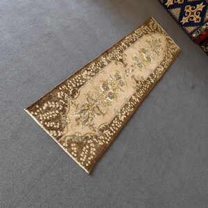 May include: A rectangular, vintage-style rug with a central beige field and intricate floral patterns in shades of brown and gold. The rug has a dark brown border with a repeating pattern of small, light-colored dots.