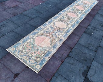 May include: A long, rectangular rug with a cream background and a repeating pattern of pink, blue, and brown floral designs. The rug has a distressed, vintage look.