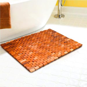 May include: A rectangular wooden bath mat with a textured surface. The mat is made of small, rectangular pieces of wood that are arranged in a grid pattern. The mat is a light brown color.