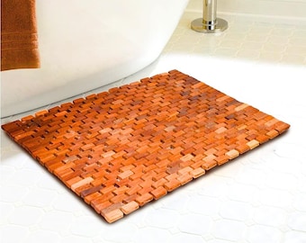 May include: A rectangular wooden bath mat with a textured surface. The mat is made of small, rectangular pieces of wood that are arranged in a grid pattern. The mat is a light brown color.