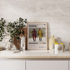 K&ouml;nnte beinhalten: Ein Filmplakat mit goldenem Rahmen, auf dem Deadpool und Wolverine in ihren Superheldenkost&uuml;men zu sehen sind. Das Plakat tr&auml;gt den Titel "Deadpool & Wolverine" und eine rote "R"-Bewertung.
