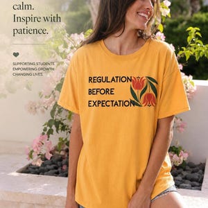 May include: A mustard yellow short-sleeved t-shirt featuring the black text "REGULATION BEFORE EXPECTATION" and a graphic of two orange tulips with green leaves. The shirt also displays the text "Lead with calm. Inspire with patience." and "SUPPORTING STUDENTS. EMPOWERING GROWTH. CHANGING LIVES."