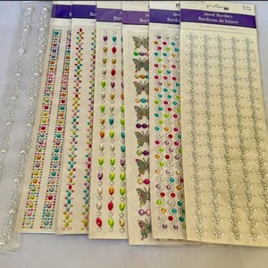 May include: A collection of self-adhesive jewel borders in various designs. The borders feature colorful rhinestones, pearls, and butterfly accents. The borders are on white backing cards and are ideal for craft projects.
