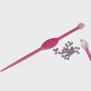May include: Pink plastic tools with a pointed end and a rounded end, along with a pile of small, silver-colored beads. One tool has a bulbous end. The tools are likely used for crafting or jewelry making.