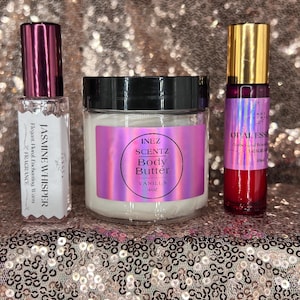 May include: A collection of beauty products, including a small perfume bottle labeled "Jasmine Whisper", a jar of "Inez Scentz Body Butter Vanilla 4oz", and a roll-on bottle of "Opal Essence Amber and Woods Fragrance". The products are arranged on a sequined surface.