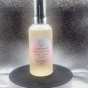 K&ouml;nnte beinhalten: Eine transparente Raumduftspr&uuml;hflasche mit silberner Kappe, beschriftet mit "Cinnamon Vanilla Mist". Das Etikett ist rosa und wei&szlig;. Die Flasche enth&auml;lt eine hellgelbe Fl&uuml;ssigkeit und ist 118 ml gro&szlig;.