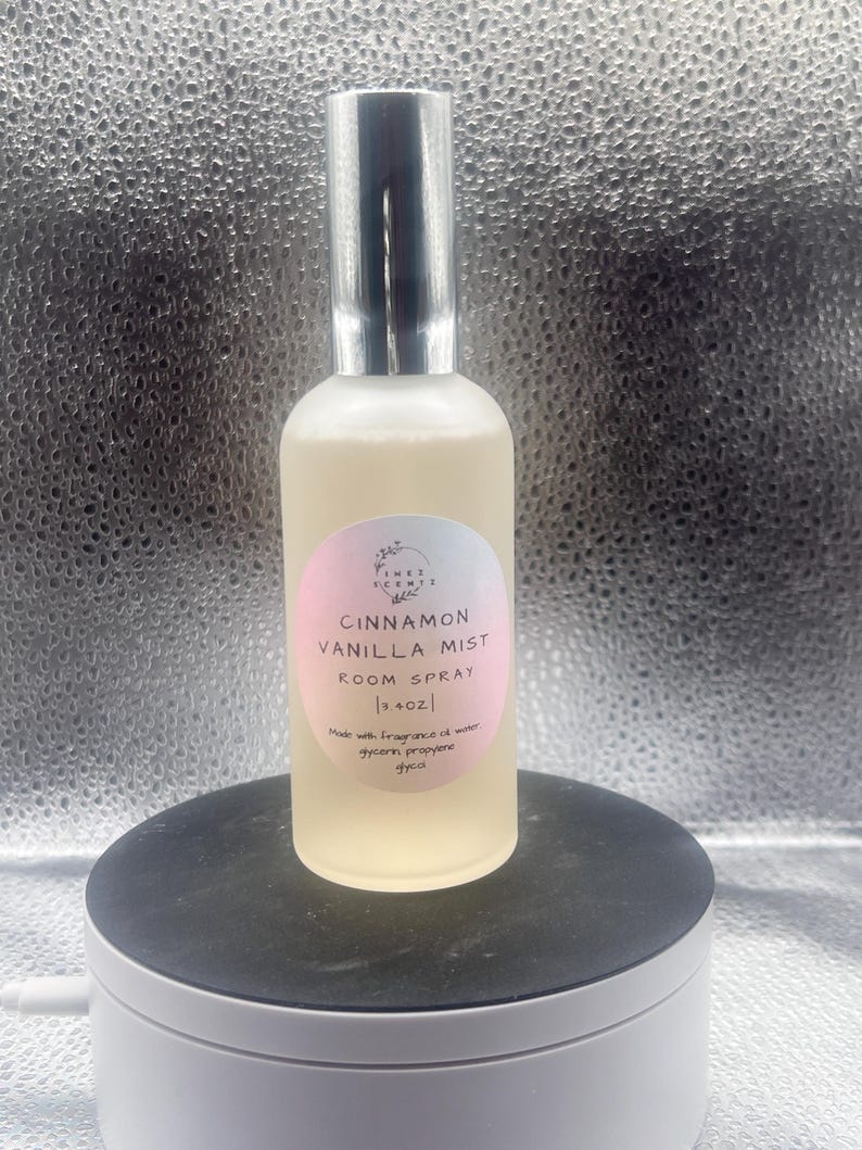 K&ouml;nnte beinhalten: Eine transparente Raumduftspr&uuml;hflasche mit silberner Kappe, beschriftet mit "Cinnamon Vanilla Mist". Das Etikett ist rosa und wei&szlig;. Die Flasche enth&auml;lt eine hellgelbe Fl&uuml;ssigkeit und ist 118 ml gro&szlig;.