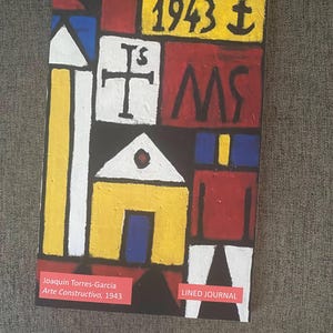 May include: A colorful abstract painting with geometric shapes in red, yellow, blue, white, and black. The painting is titled "Arte Constructivo, 1943" and is by Joaquin Torres-Garcia. The painting is on a lined journal cover.