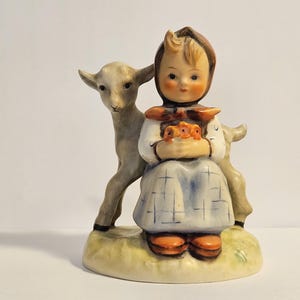 May include: A porcelain figurine of a girl in a blue and white dress holding a bouquet of flowers, with a gray goat beside her.