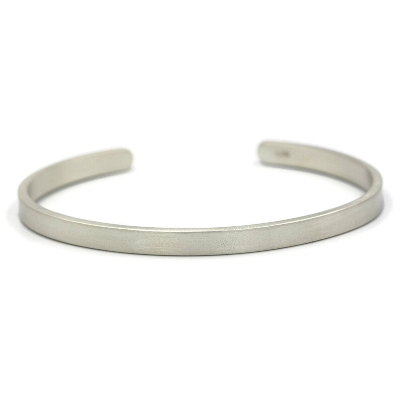 Puede incluir: Una pulsera de pu&ntilde;o de color plateado con un dise&ntilde;o plano y rectangular. La pulsera tiene un acabado mate y un estilo simple y minimalista. El dise&ntilde;o abierto permite pon&eacute;rsela y quit&aacute;rsela f&aacute;cilmente. Esta joya es adecuada para el uso diario.