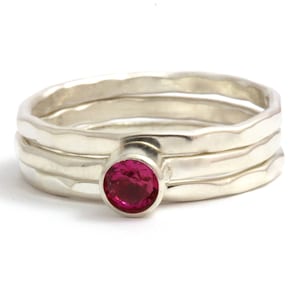May include: A set of three silver rings with a hammered finish. The top ring features a bright pink gemstone.