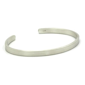 Puede incluir: Una pulsera de plata con un dise&ntilde;o minimalista. La pulsera abierta tiene un perfil plano y rectangular y un acabado liso y mate. El extremo de la pulsera tiene la marca "925".