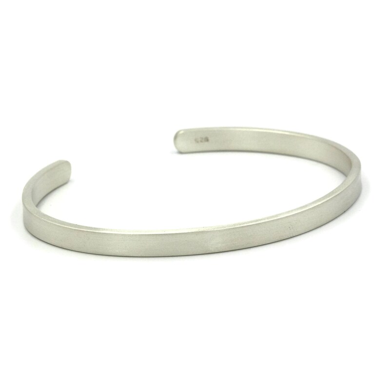 Puede incluir: Una pulsera de plata con un dise&ntilde;o minimalista. La pulsera abierta tiene un perfil plano y rectangular y un acabado liso y mate. El extremo de la pulsera tiene la marca "925".