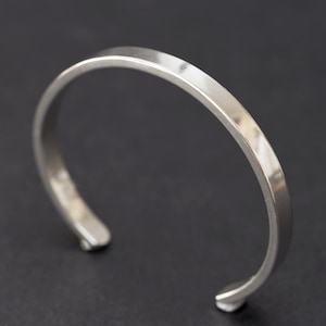 Puede incluir: Una pulsera de pu&ntilde;o plateada con la parte superior plana y bordes redondeados. El dise&ntilde;o abierto permite un f&aacute;cil uso. La pulsera est&aacute; hecha de un material met&aacute;lico brillante.