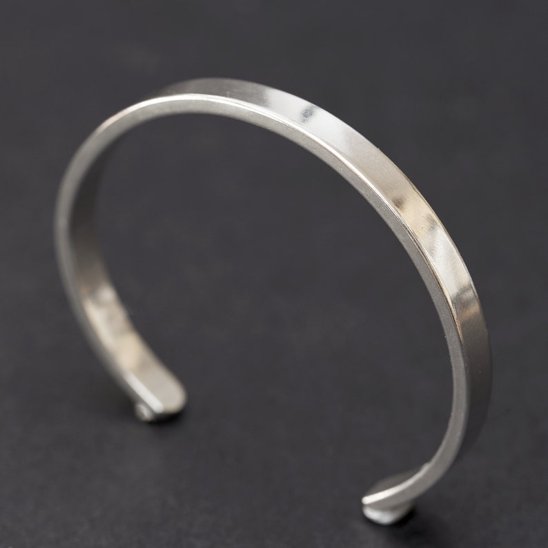 Puede incluir: Una pulsera de pu&ntilde;o plateada con la parte superior plana y bordes redondeados. El dise&ntilde;o abierto permite un f&aacute;cil uso. La pulsera est&aacute; hecha de un material met&aacute;lico brillante.