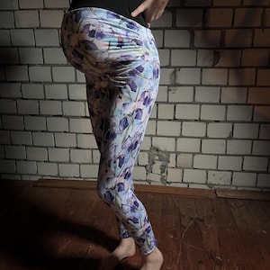 May include: A pair of floral leggings with a light blue background and purple flowers. The leggings are fitted and have a high waist.