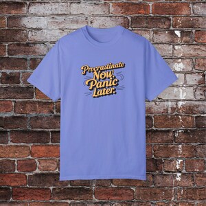 Könnte beinhalten: Ein hellblaues T-Shirt mit dem Text "Procrastinate Now, Panic Later." in einer retro-orangenen Schrift.