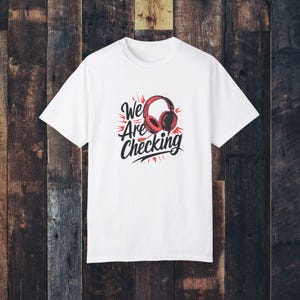 Puede incluir: Camiseta blanca con un diseño gráfico de auriculares rojos y el texto "We Are Checking" en negro.