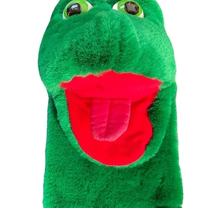 May include: A green plush hand puppet shaped like a frog. The puppet has large, round green eyes, a red mouth, and a red tongue. The puppet is made of soft, fuzzy material.