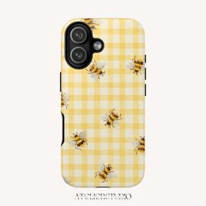 Puede incluir: Funda de teléfono a cuadros amarillos y blancos con un patrón de abejas de acuarela. La funda tiene una lente de cámara y botones negros. El texto "ATCLIERSTUDIO" está impreso en la parte inferior.