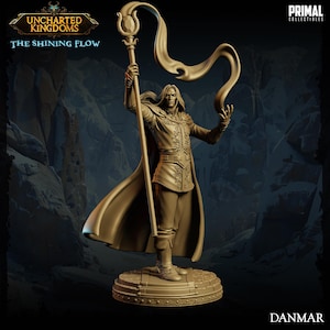 May include: A gold-colored miniature figurine of a man holding a staff with a flowing fabric attached to the top. The figurine is standing on a round base with a detailed design. The text "Uncharted Kingdoms: The Shining Flow" and "Danmar" are visible in the image.