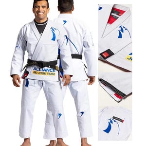 Puede incluir: Uniforme blanco de Jiu-Jitsu con detalles azules y negros. El uniforme presenta el logotipo de Alliance Jiu Jitsu Team y un cinturón negro. La chaqueta tiene un diseño de águila azul en la parte delantera y trasera. Los pantalones tienen un diseño de rayo azul.