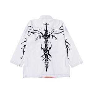 Pode incluir: Uniforme branco de artes marciais com um design gráfico preto marcante nas costas. O design apresenta um intrincado motivo estilizado de espada ou cruz. O uniforme tem uma gola tradicional e costuras reforçadas.