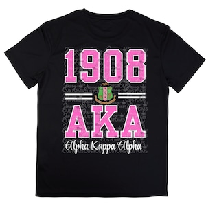 May include: Black t-shirt with pink text that reads "1908 AKA Alpha Kappa Alpha". The text is surrounded by a pattern of the words "CUSTOMS" and "Jairy".