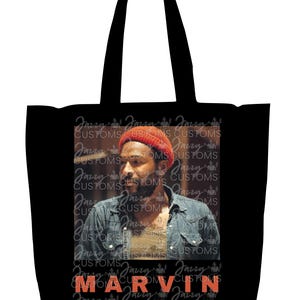 May include: Black tote bag featuring a portrait of a man wearing a red beanie and denim jacket. The name "MARVIN" is printed in orange block letters below the portrait. The background includes the text "Jazzy Customs" repeated.