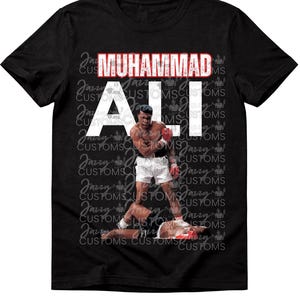 May include: Black t-shirt featuring a graphic of Muhammad Ali in a boxing match. The text "MUHAMMAD ALI" is displayed in white and red. The shirt has a crew neck and short sleeves.