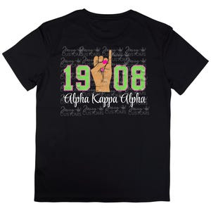 Może przedstawiać: Czarny T-shirt z zielonym i białym nadrukiem "1908" i tekstem "Alpha Kappa Alpha" w kolorze białym. Nadruk zawiera rękę z różowymi paznokciami wykonującą znak "ok".
