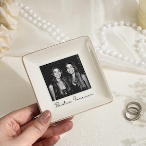 May include: A square, off-white ceramic trinket dish with a gold rim. The dish features a black and white photo of two smiling women and the text "Bestie Forever".