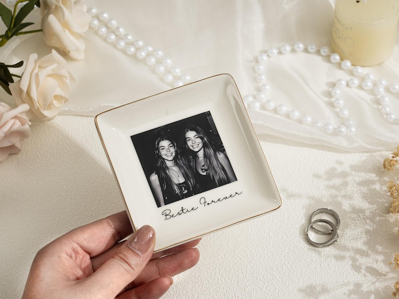 May include: A square, off-white ceramic trinket dish with a gold rim. The dish features a black and white photo of two smiling women and the text "Bestie Forever".