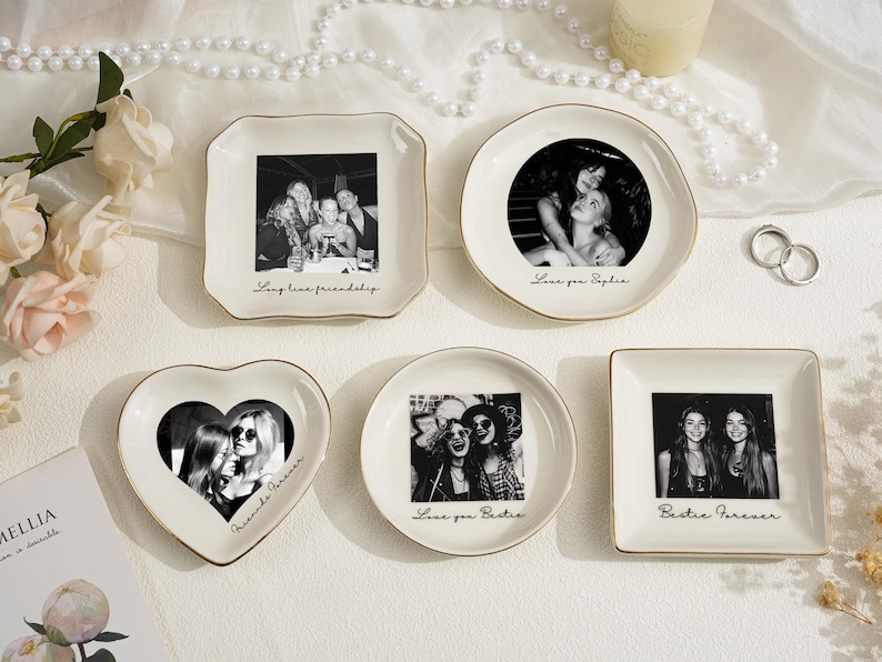 May include: A collection of personalized ceramic trinket dishes in various shapes, each featuring a black and white photograph. The dishes have gold trim and include phrases like "Love you Sophie" and "Bestie Forever."