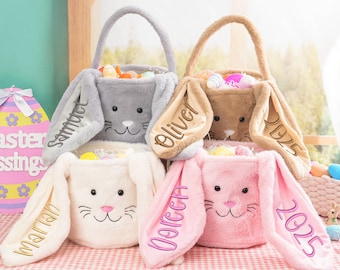 Puede incluir: Cuatro cestas de Pascua de peluche con forma de conejo con orejas largas y caídas. Las cestas son grises, marrones, blancas y rosas. Cada cesta tiene un nombre bordado en la oreja:  "Samuel", "Oliver", "Dorcen" y "Marian". Las cestas están llenas de huevos de Pascua y dulces.